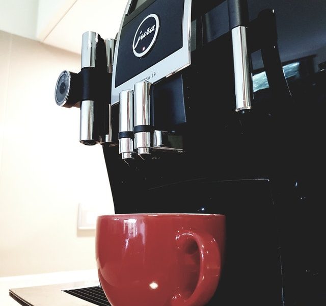 mesin kopi warna hitam dengan cangkir merah dibawahnya